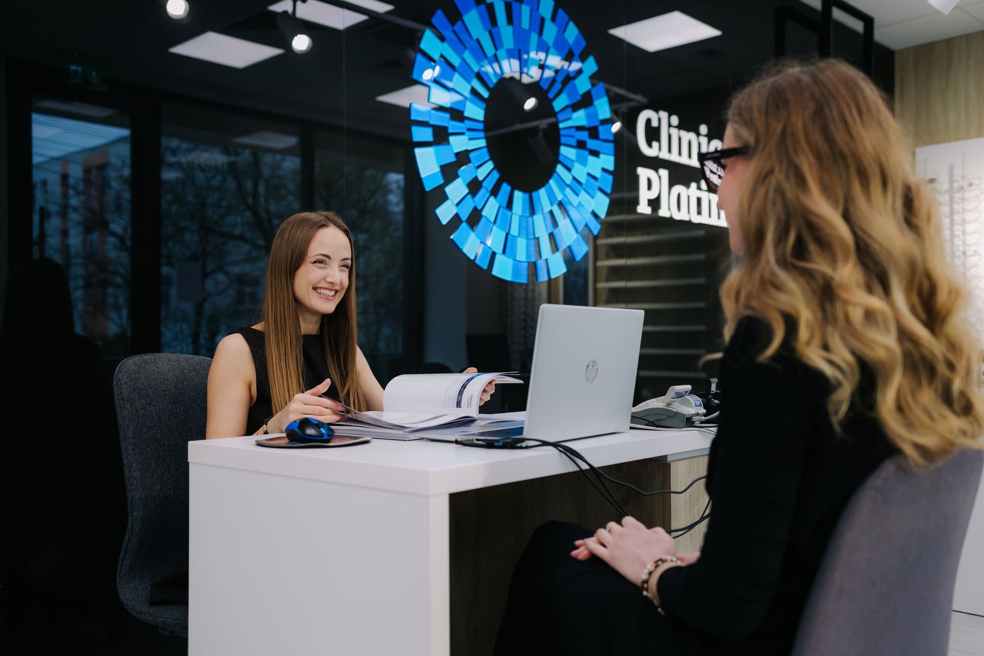 Consilier Platinum Optic discutând cu o pacientă, sub logo-ul luminos al clinicii